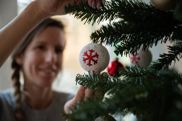 年轻的女人在圣诞树上挂着红白相间的节日礼物 注意球的方向 — 图库照片