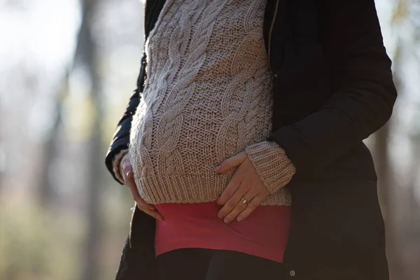 Closeup view of a pregnant woman touching her swollen belly in winter clothes standing outside in nature.