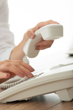 Beyaz sabit hatlı telefondan bir kadının telefon numarasını çevirişinin yakın görüntüsü..