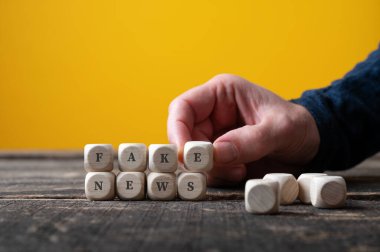 Erkek el sahte haber işareti yapmak için tahta küpleri birleştiriyor. Sarı arkaplan.