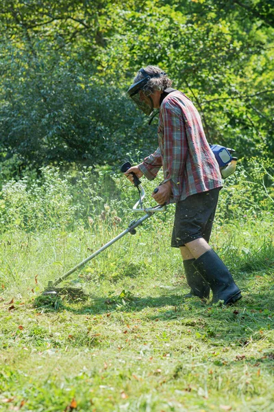 シニア男身に着けている保護ヘルメットでゴーグルを身に着けている間彼の目を守るために草を刈る雑草の食べる — ストック写真