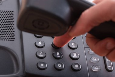 Siyah sabit hatlı bir telefondan telefon numarası çeviren bir parmağın yakın plan görüntüsü.