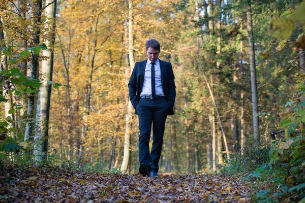 美しい秋の森を歩くエレガントなビジネススーツの若いビジネスマン — ストック写真