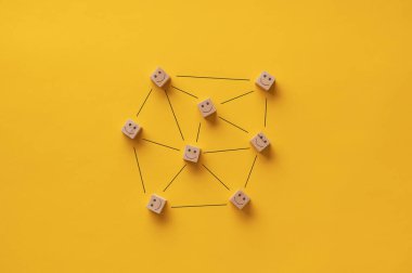 Elle çizilmiş çizgilerle birbirine bağlı birçok tahta bloğa çizilmiş gülen mutlu yüz simgeleri. Sarı arkaplan.