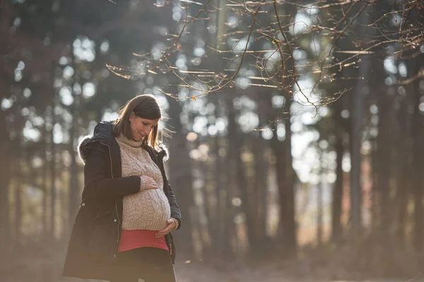 妊娠中の若い女性は森の中に立って感動し 彼女の腹を愛して見て — ストック写真