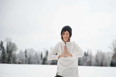 Peaceful young woman meditating with her hand joined in front of her chest standing outside in beautiful snowy winter nature.
