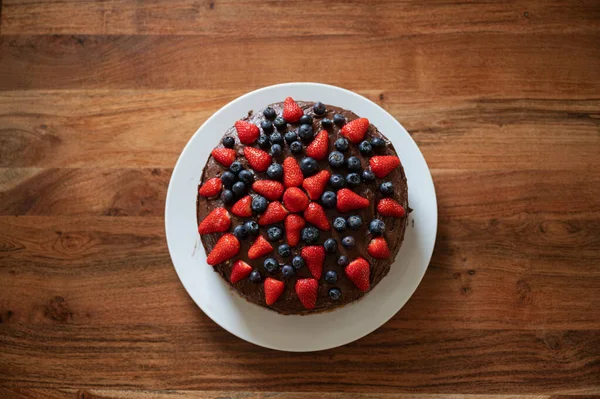 新鮮なブルーベリーとイチゴで飾られたおいしいビーガンチョコレートケーキのトップビュー — ストック写真