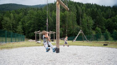 İki bebek, erkek ve kız kardeş, dışarıda oyun alanında sallanmak gibi özel bir atlıkarıncaya biniyorlar..