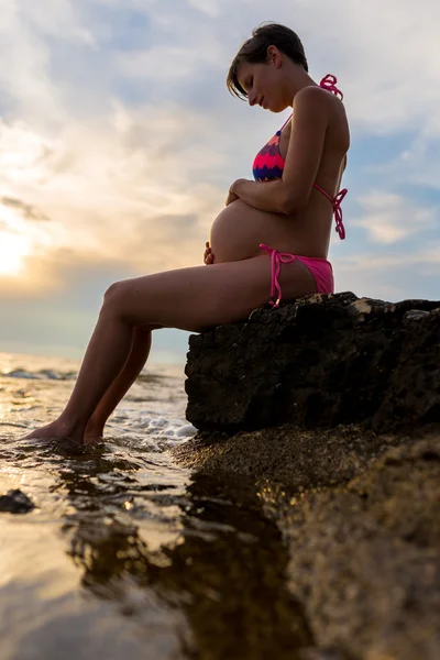 Kobieta w ciąży sobie Bikini siedząc na brzegu — Zdjęcie stockowe
