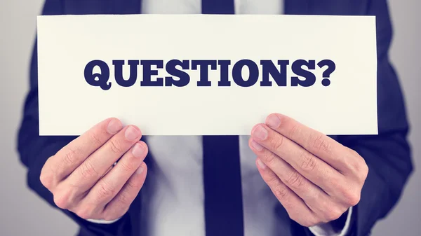 Empresario sosteniendo Preguntas signo hacia usted — Foto de Stock