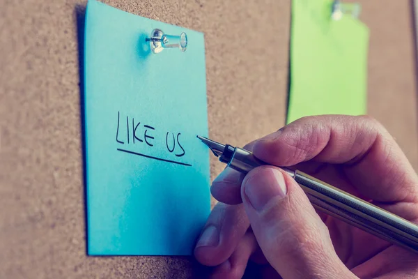 Man writing - Like Us - on a notice board — Stock Photo, Image