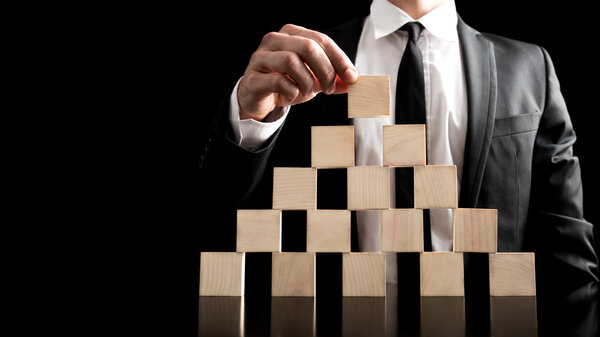 Бизнесмен строит деревянные блоки к пирамиде
