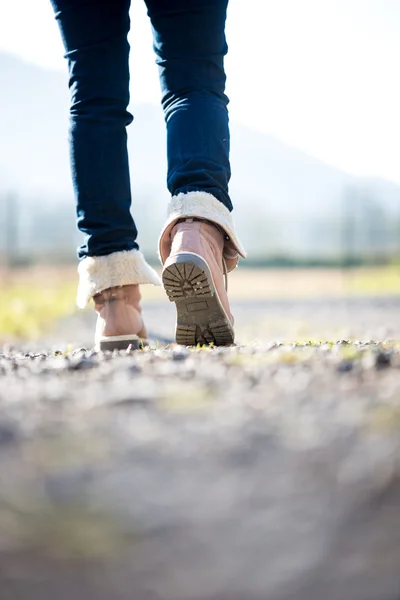 Femme en jeans et bottes marchant le long d'un chemin rural — Photo