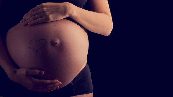 Der nackte geschwollene Bauch einer schwangeren Frau, die an ihren Händen gestülpt wird — Stockfoto