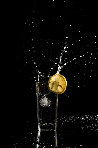 Água salpicando para fora de um copo como um cubo de gelo é deixado cair em um — Fotografia de Stock