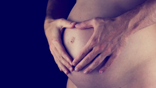 Manliga händer som håller henne gravid mage — Stockfoto