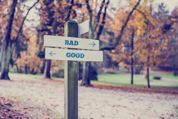 Cartel de madera rústica en un parque de otoño con las palabras Malo - Bueno — Foto de Stock