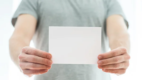 Man in a grey t-shirt holding a blank card — Stock Photo, Image