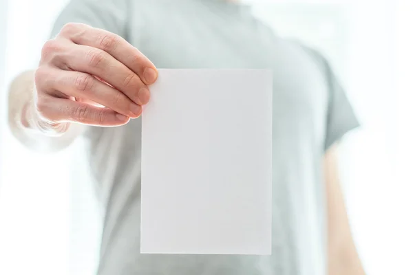 Homem com uma camiseta cinzenta segurando um pedaço de papel branco em branco — Fotografia de Stock