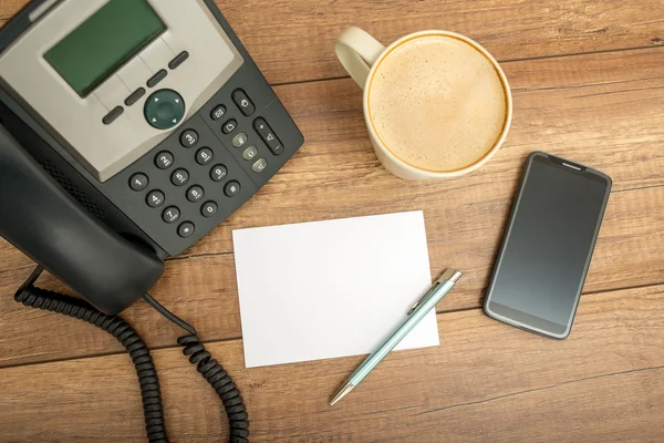 Desk phone, paper and a smart phone, on a table — Stockfoto