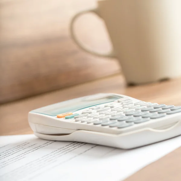 White desk calculator on a document next to a mug — 图库照片