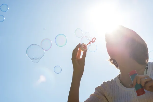 Young woman joyfully blowing a stream of soap bubbles. — Stock Photo, Image