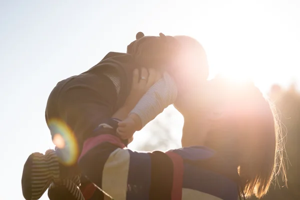 Mujer besando bebé retroiluminado por la luz del sol brillante —  Fotos de Stock