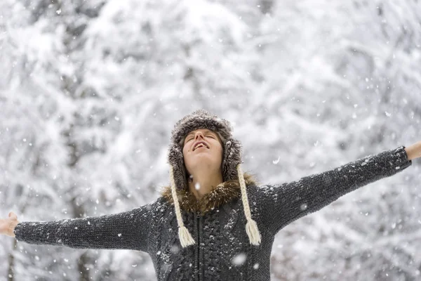 Mujer de pie al aire libre en la nieve que cae con los brazos extendidos —  Fotos de Stock