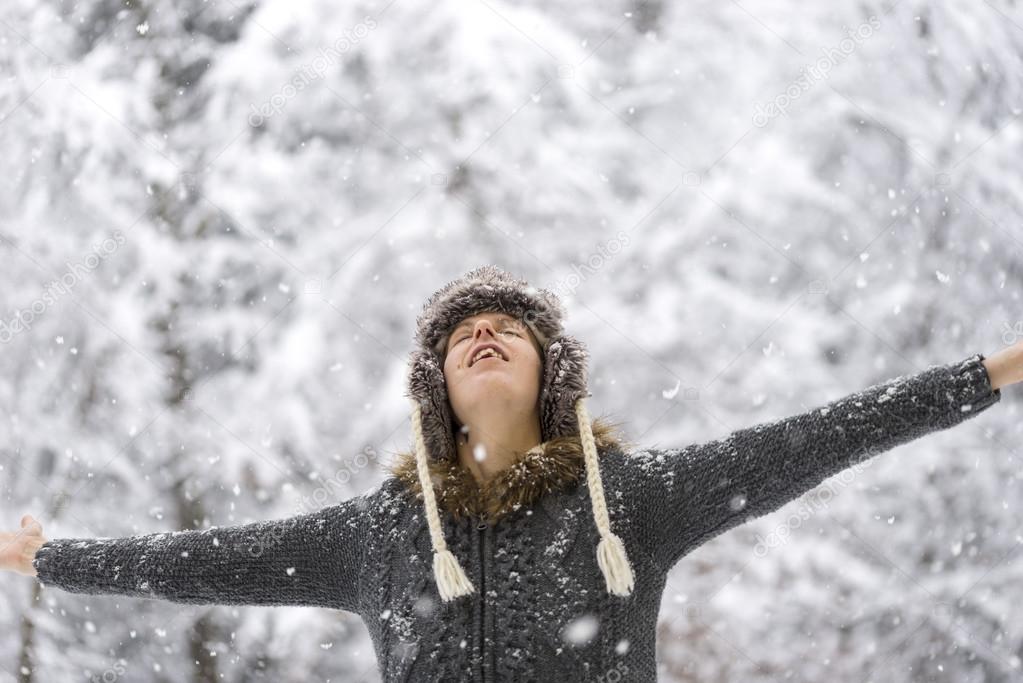 Woman standing outdoors in falling snow with her arms outspread