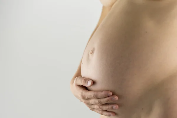 Closeup of pregnant woman holding her bare swollen belly — Zdjęcie stockowe