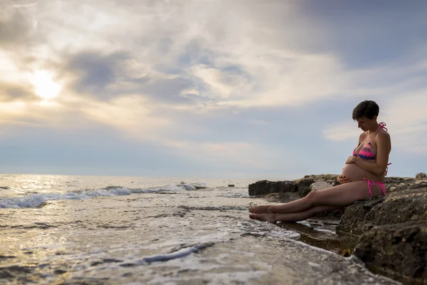 Pregnant woman in ninth month of pregnancy sitting on a rock by — Stock Photo, Image