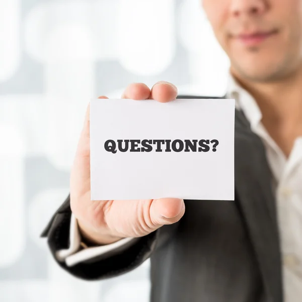 Businessman holding up a small white card saying Questions — Stock Photo, Image