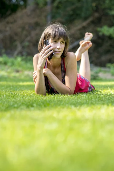 Barefoot young woman chatting on a mobile phone as she lies on h — Stock Fotó