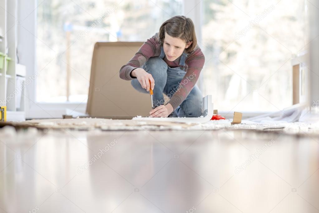 Young Woman assembling a DIY furniture at home kneeling on the f