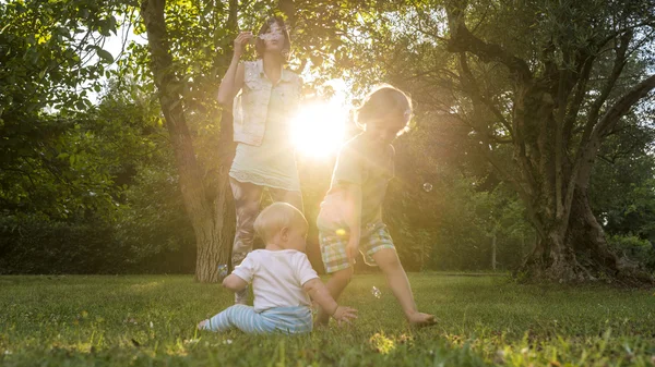 Счастливая молодая мать, пускающая мыльные пузыри, играя со своим ребенком, как — стоковое фото