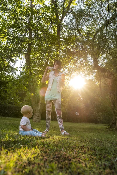 Cheerful young mother blowing soap bubbles towards  her baby boy — Stockfoto