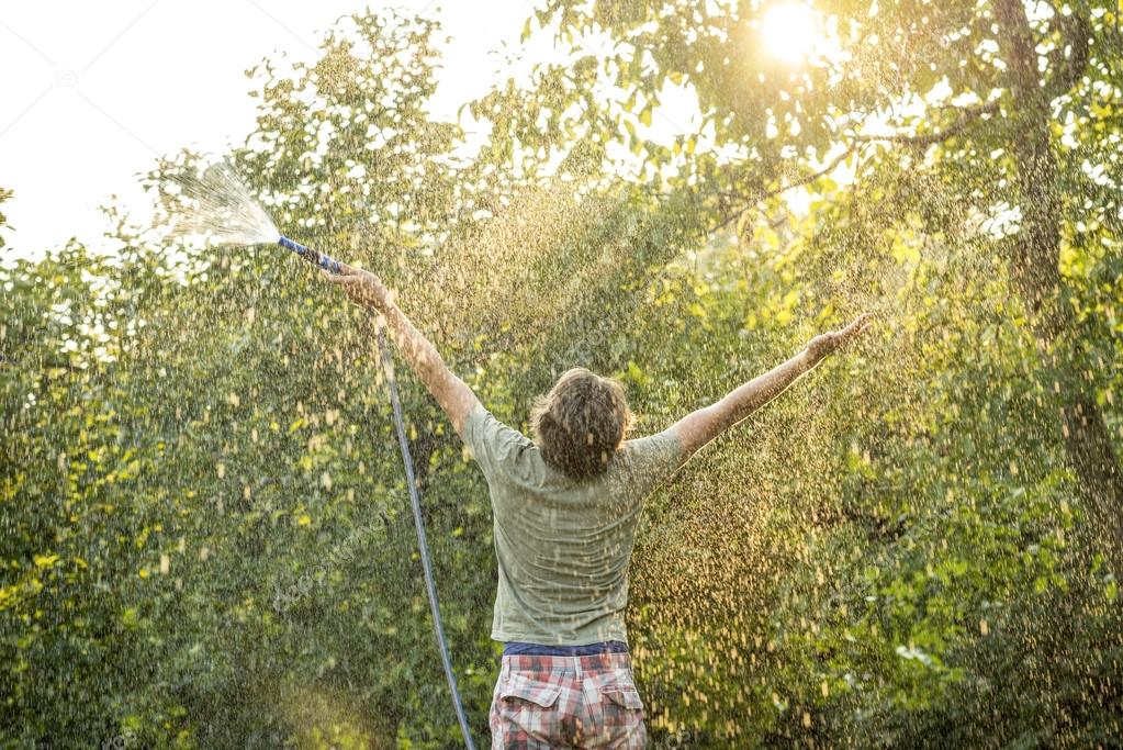 Man with Garden Hose Raises his Arms for Happiness