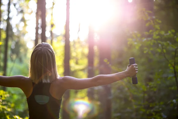 Jovem mulher loira trabalhando com halteres em bela natur — Fotografia de Stock