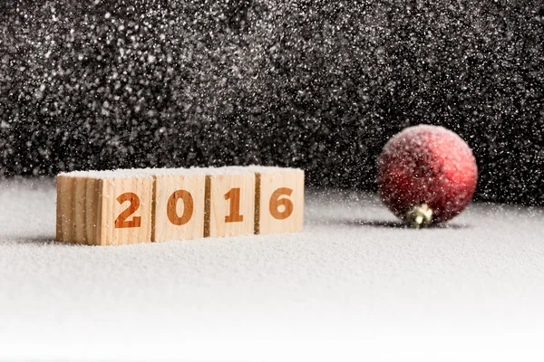 2016 assine em cubos de madeira e bola de Natal vermelho deitado em uma neve — Fotografia de Stock
