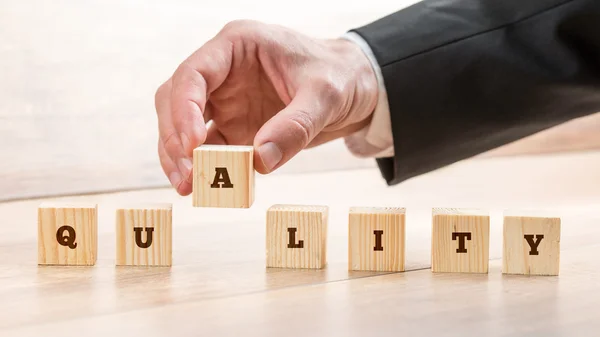 Unternehmer montiert das Wort Qualität mit sieben Holzwürfeln — Stockfoto