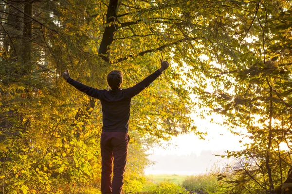 Junger Mann steht am Waldrand und hebt die Arme — Stockfoto