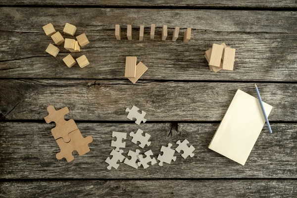 Bloco de notas em branco, lápis e pilhas de peças de quebra-cabeça, blocos de madeira — Fotografia de Stock