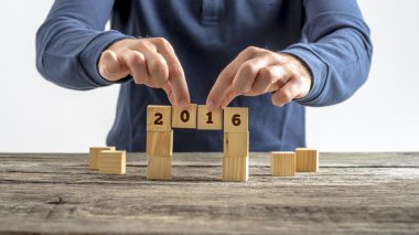 Person building a bridge of wooden cubes with the year 2016 sign