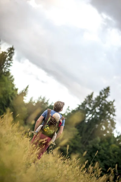 Junger Vater, der seinen Sohn auf dem Rücken trägt, während sie durch ein — Stockfoto