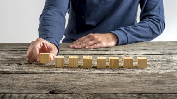 Vista frontal de um homem colocando oito cubos de madeira em branco em uma fileira — Fotografia de Stock