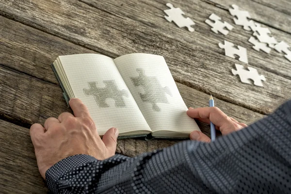 Man sketching two matchng puzzle pieces in his notepad — Zdjęcie stockowe