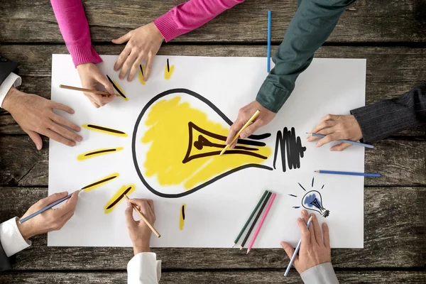 Six people, men and women, drawing bright yellow light bulb on a — Stock Photo, Image