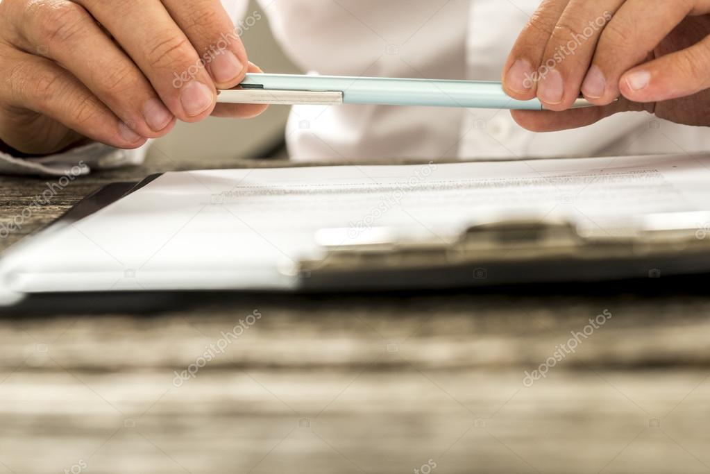 Closeup view of male hands holding pencil over paperwork on clip