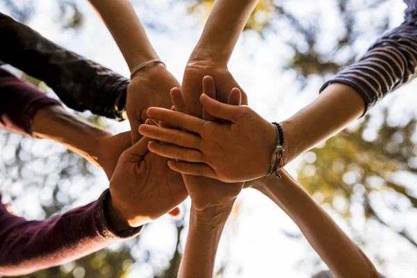 Shot from below of four people stacking hands outside in nature — Stock Photo, Image