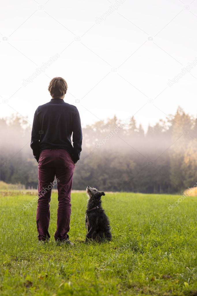 Young man standing in the middle of green meadow with his black
